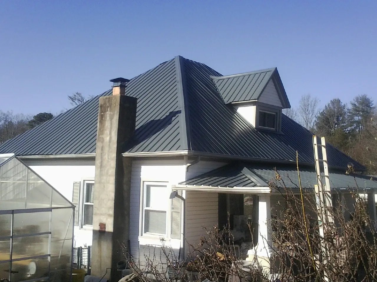 Dark blue standing seam metal roof on a white farmhouse with dormer — Slate & Tile Roof Repair by Roofing Brothers in Howell