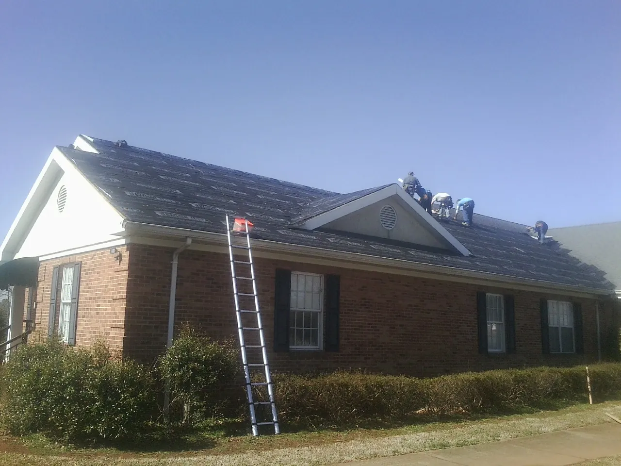 Crew tearing shingles off a brick ranch roof with a ladder set — Emergency Roof Repair work by our crew in Howell
