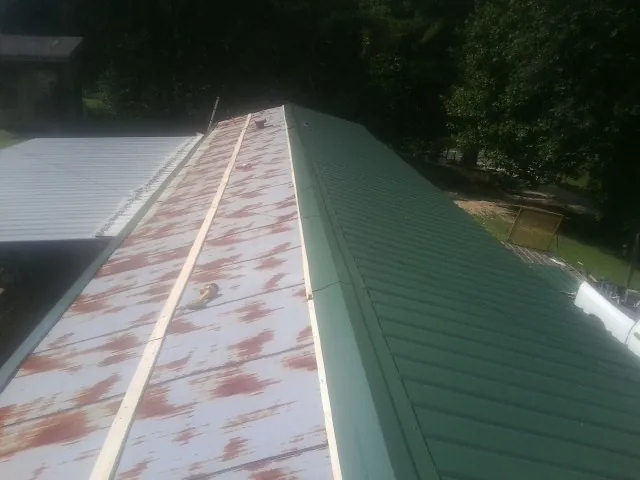 Old rusted panels beside newly installed green metal roofing — Wind Damage Roof Repair by Roofing Brothers in Howell